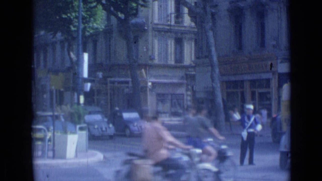 Scooters and cars move through a city street while a policeman stands at the roadside.
