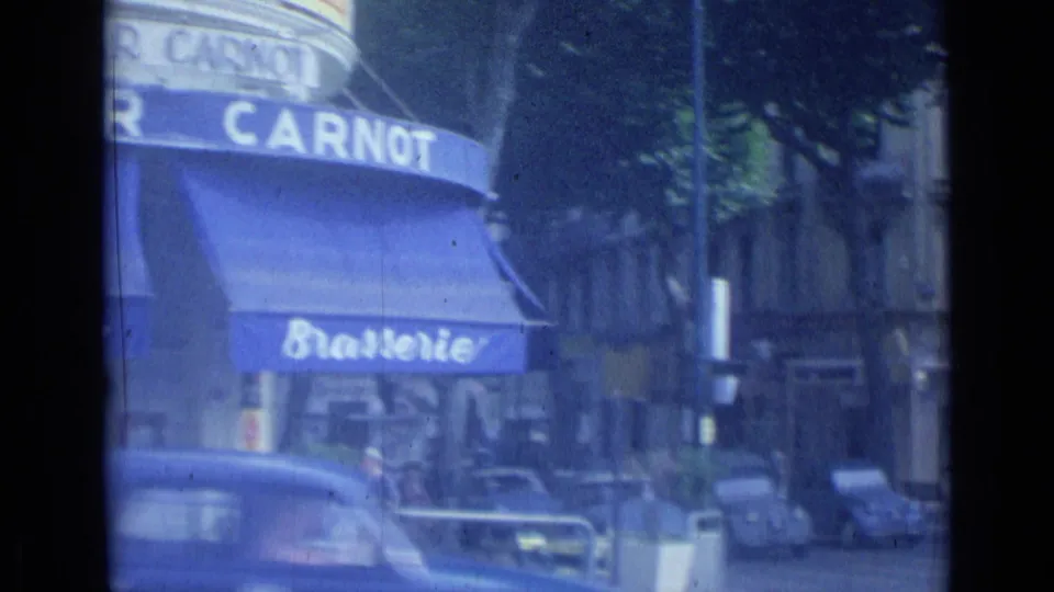 A Cannes street corner shows the blue Brasserie Carnot awning, cars, trees, and storefronts in soft 8mm color.