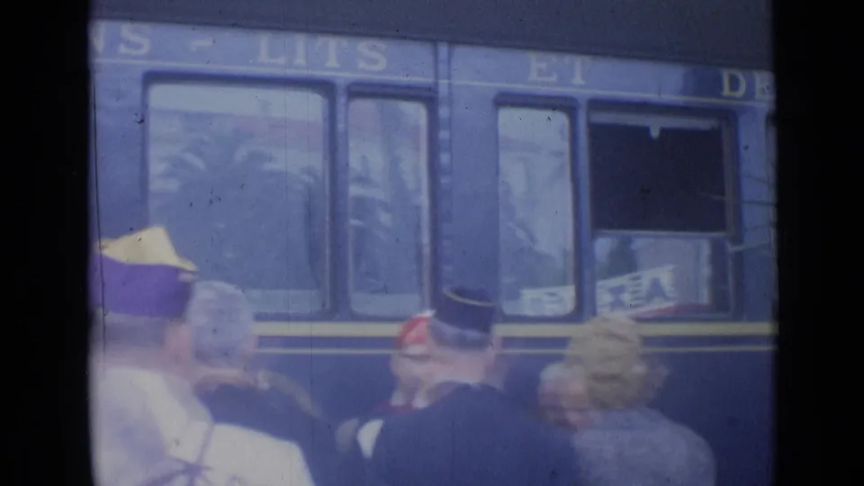 1962 Cannes platform view of a blue train moving past waiting people, with partial lettering and carriage windows visible.