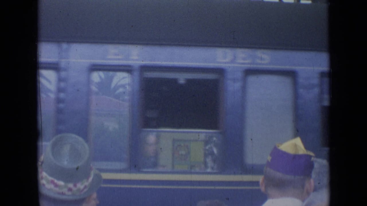Train carriage window and platform figures seen beneath station roof.