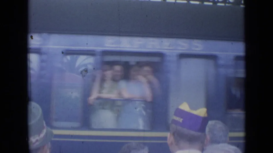 Passengers appear in a blue train window while waiting people, including a purple and yellow cap, stand on the Cannes platform.