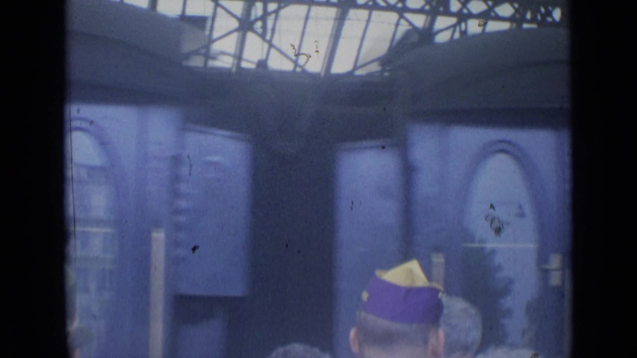 Blue train carriage behind a station crowd, with purple-and-yellow caps in the foreground.
