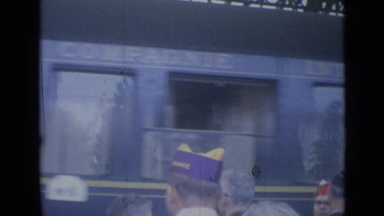 Train windows pass behind a crowd, with a purple cap and a red cap visible at right.