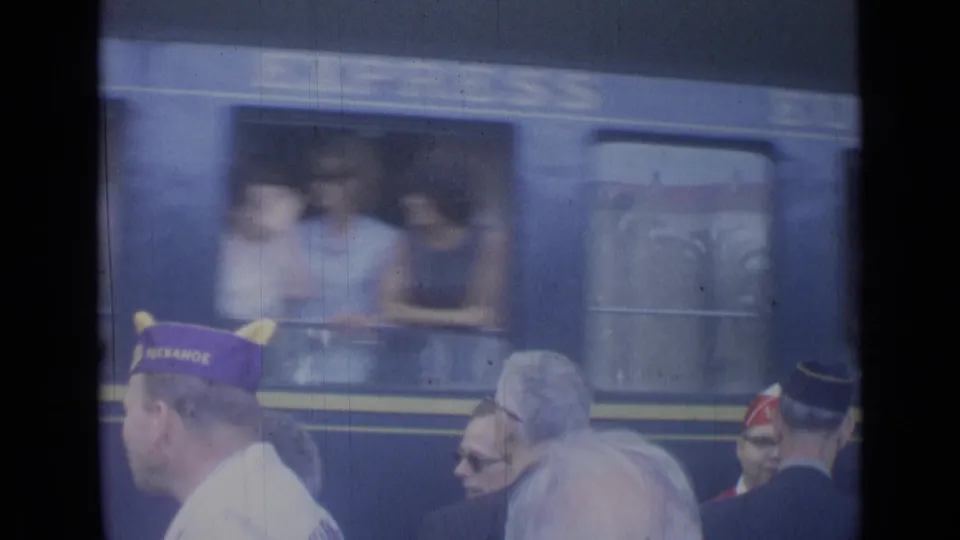 1962 Cannes station platform with men in distinctive caps near a blue train as passengers lean from open windows.