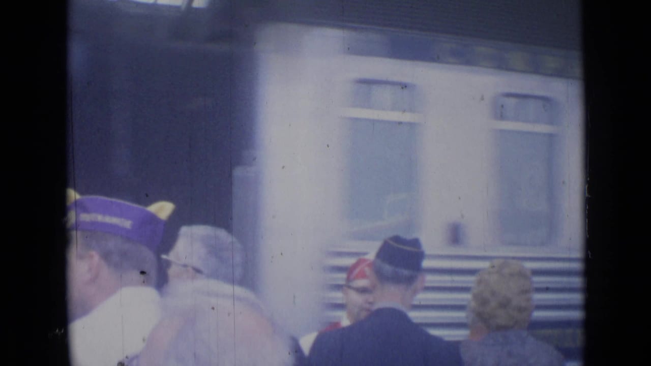 Cannes railway platform scene showing capped men, suited travelers, and train windows during a public greeting in 1962.