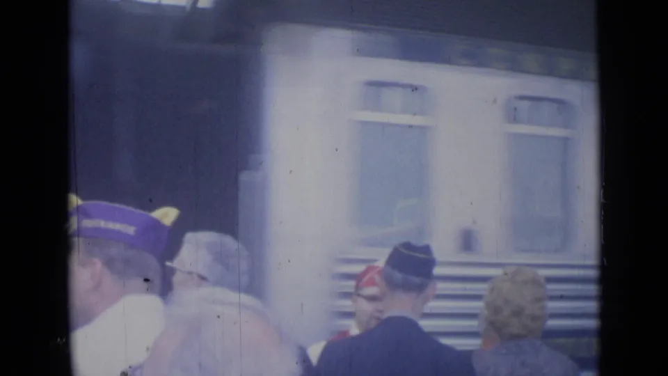 Cannes railway platform scene showing capped men, suited travelers, and train windows during a public greeting in 1962.