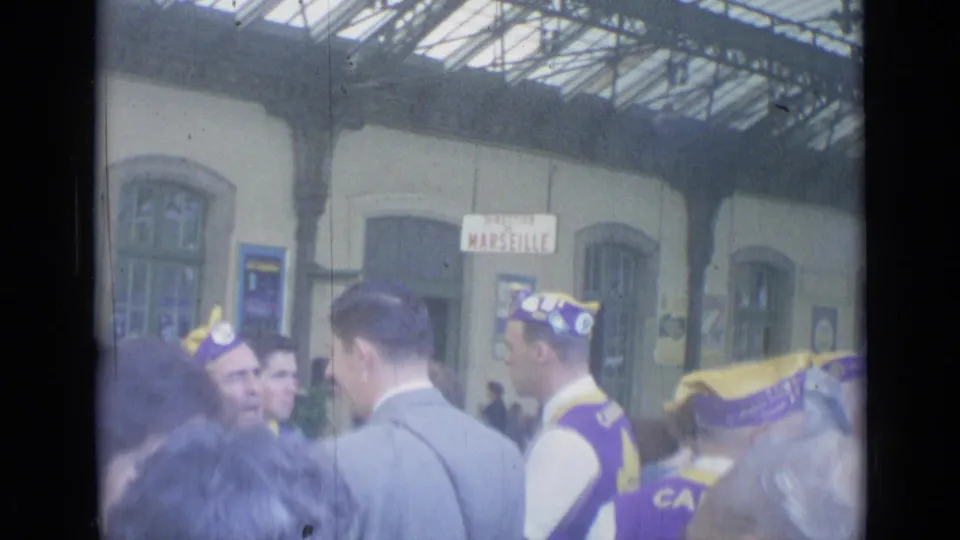 Group of men in matching purple and yellow clothing gathered beneath station roofing near a Marseille sign in Cannes, France.