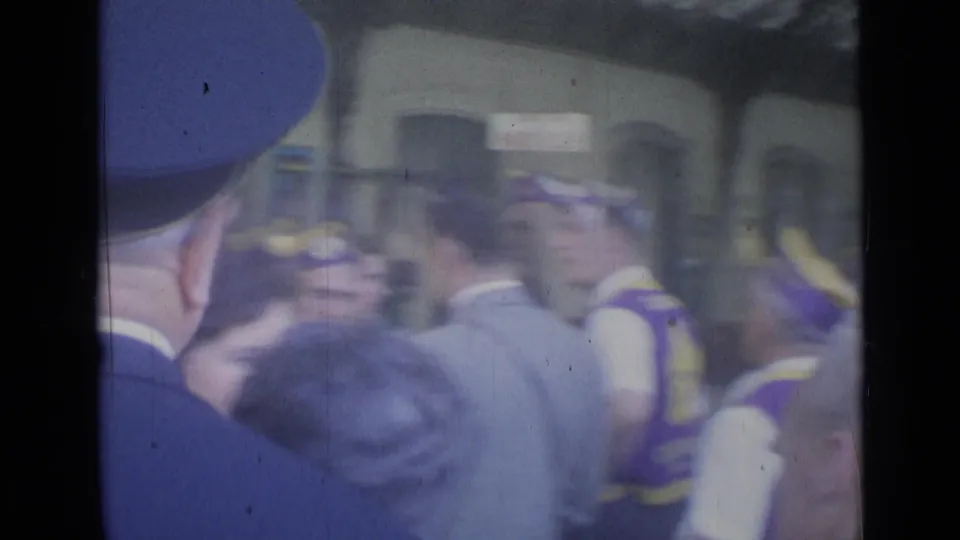 Handheld 8mm view of a Cannes station crowd, with a uniformed railway figure and destination signage partly visible.