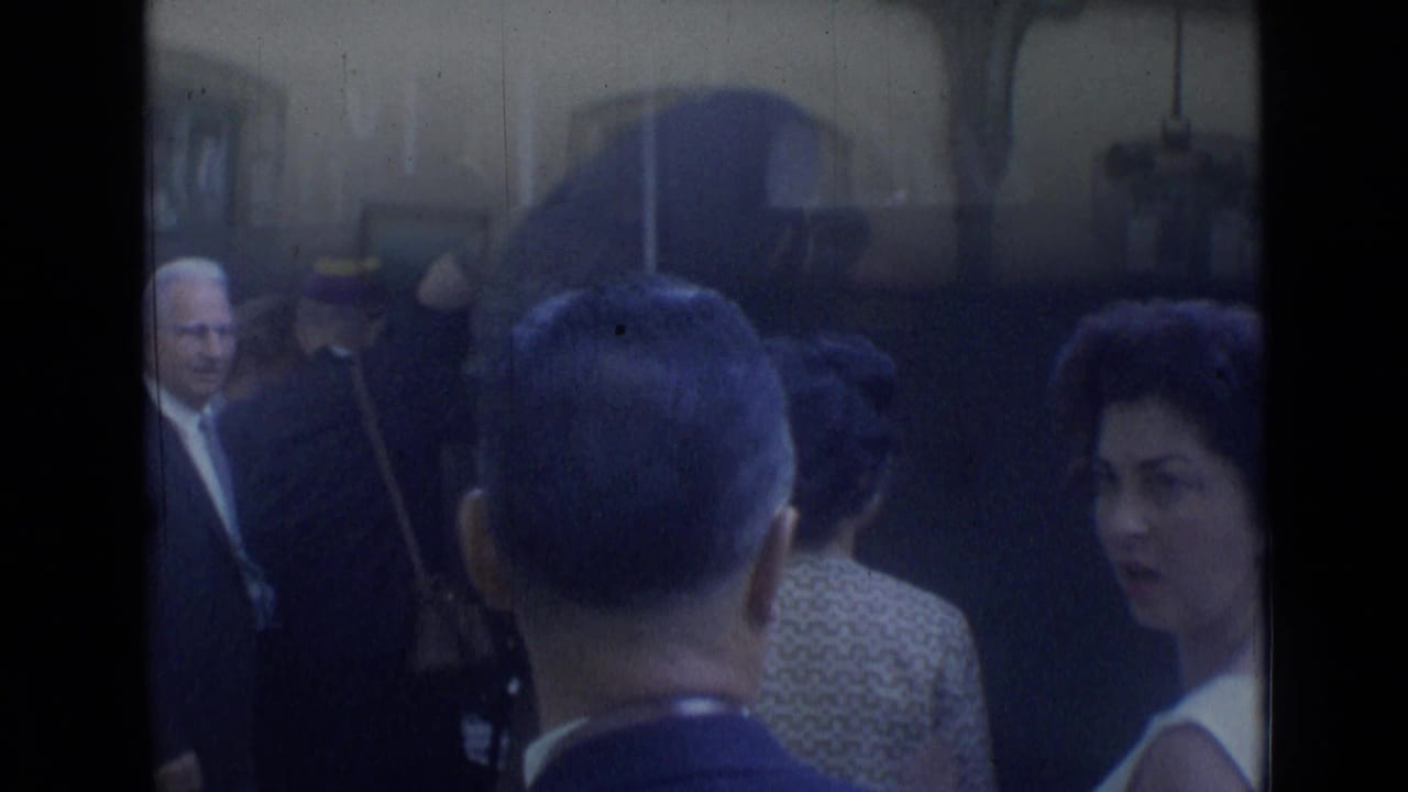 Crowd inside a station area with suited men and a woman turning toward the camera.