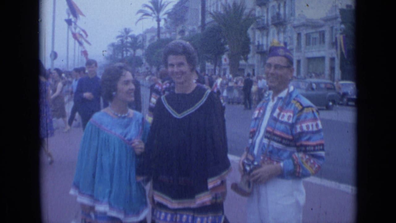 Cannes, France, 1962 street parade with two women in blue and black garments beside a man in patterned dress holding a camera.