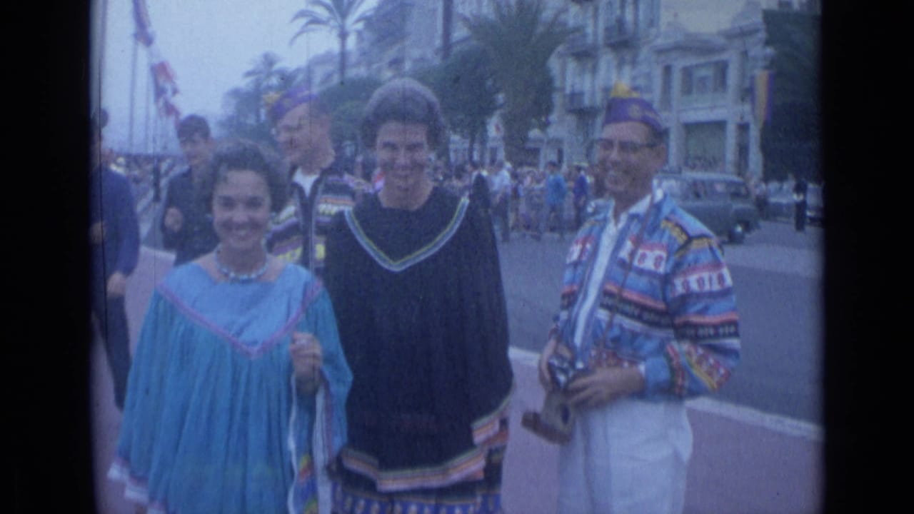 Costumed participants face the camera on a city street with palm trees, cars, and a crowd in the background.