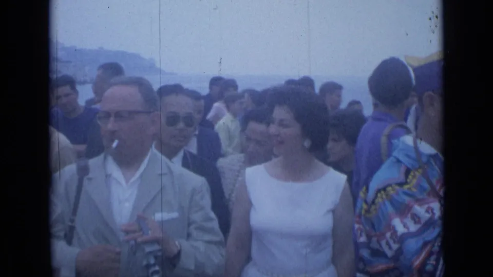 Cannes, France, 1962 parade crowd with formally dressed spectators, a man holding a camera, and a costumed participant at right.