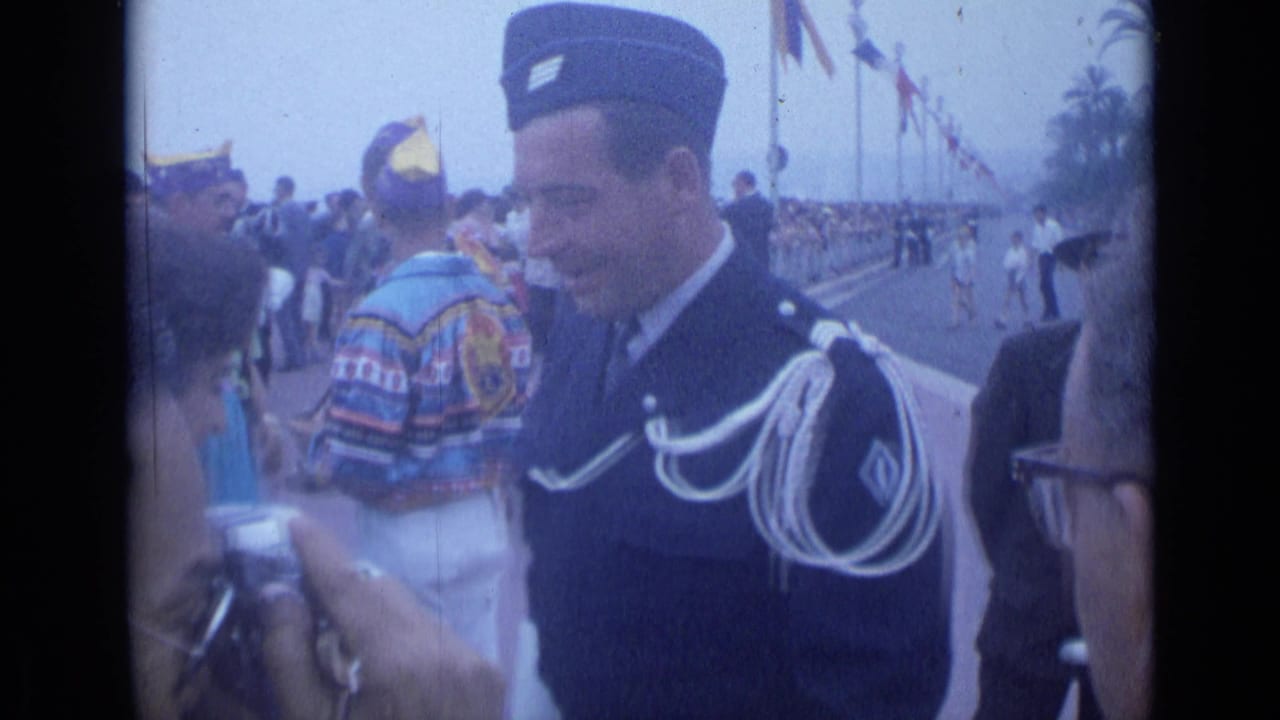 Uniformed man smiles beside a crowd while a foreground person raises a camera.