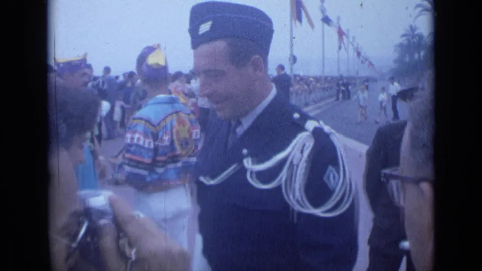 In Cannes, France in 1962, a uniformed man with white shoulder cords smiles near spectators on a flagged promenade.