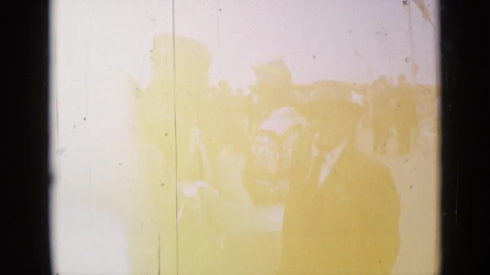 1962 Cannes home-movie frame with a dark-suited man near parade spectators, partly obscured by yellow fading and scratches.