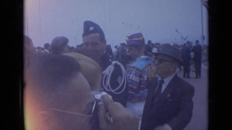 1962 Cannes frame showing men in formal uniforms and ceremonial attire near a crowd, with a photographer's head and camera in the foreground.