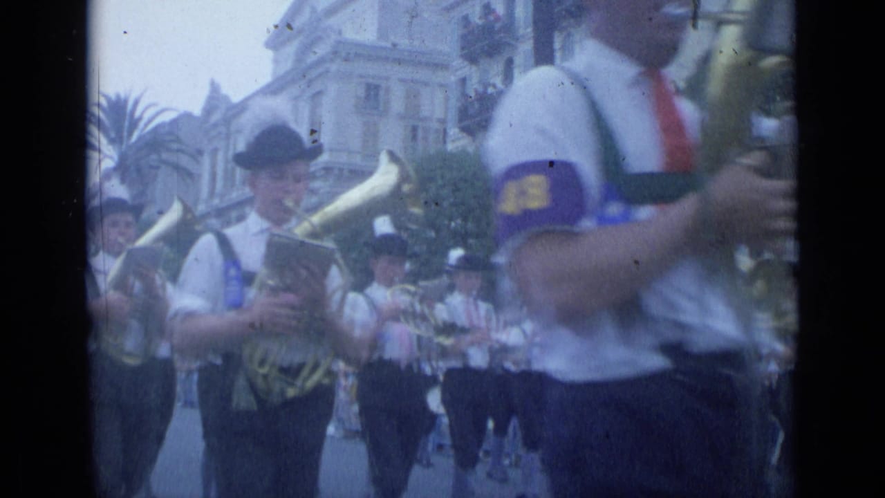 A tuba player and other band members pass close to the camera.