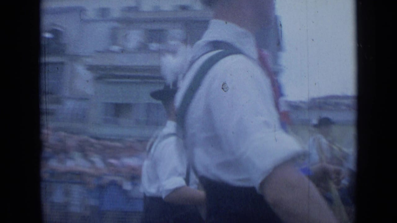 1962 Cannes home-movie frame showing a young drummer from behind beside a street parade and spectators.