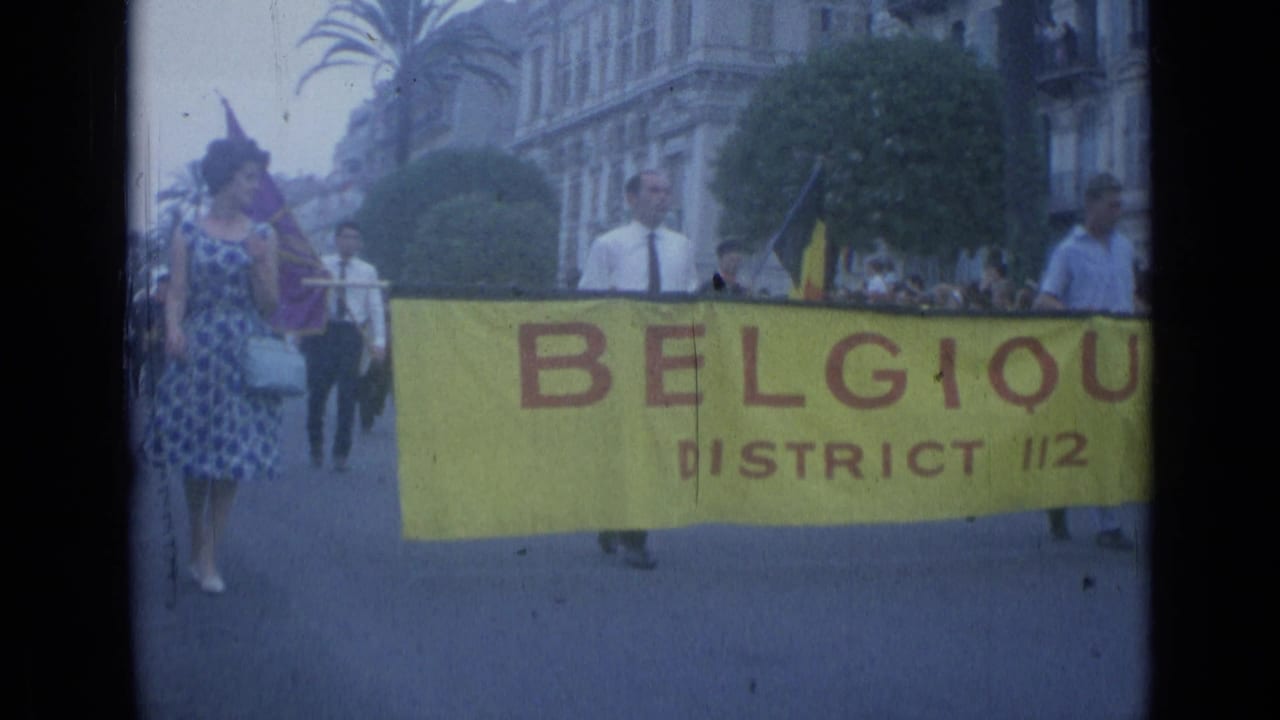 Marchers carry a yellow Belgique District 112 banner along a city street.