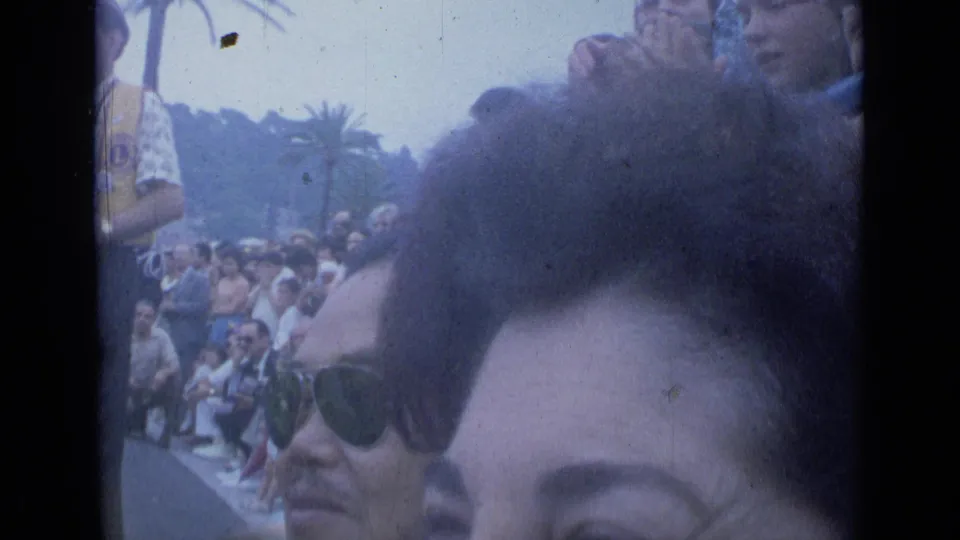 1962 Cannes spectator view with a man in aviator sunglasses in the foreground and seated or standing onlookers behind him.