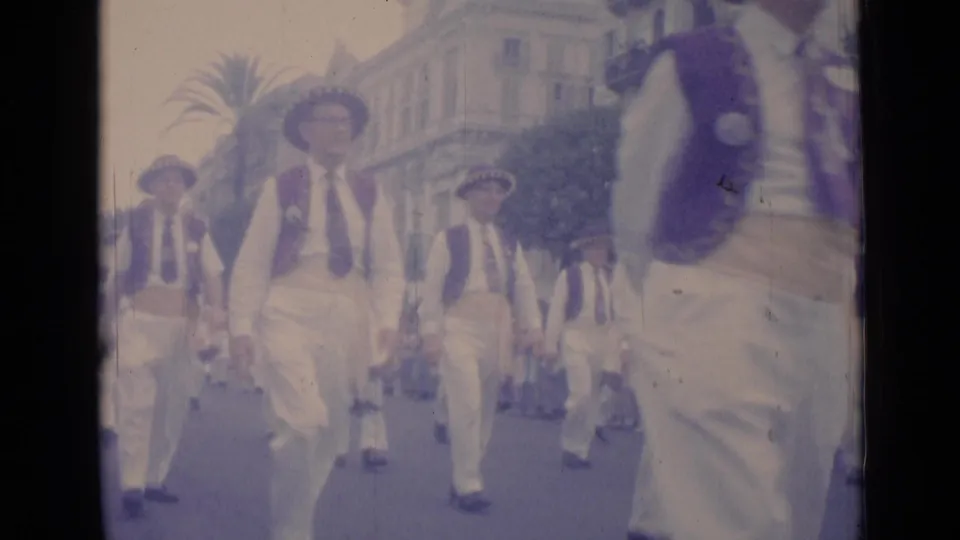 Street-level 8mm view in Cannes, 1962, with a costumed marcher passing close while others continue in formation behind him.