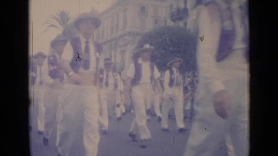 1962 Cannes home-movie frame of the parade continuing, with matching outfits, visible spectators and soft faded 8mm color.