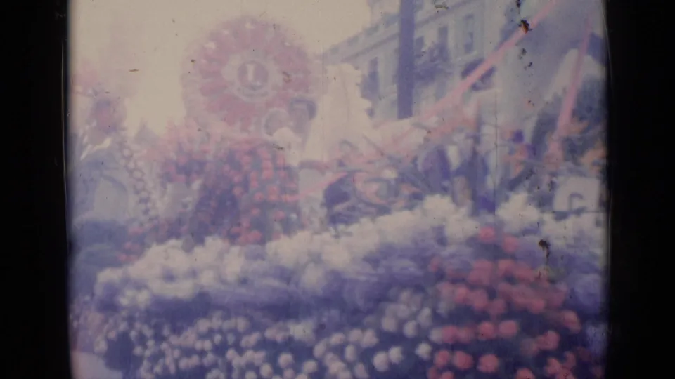 A Cannes carnival float appears covered in red, white, and purple flowers with a circular Lions Club emblem above the display.