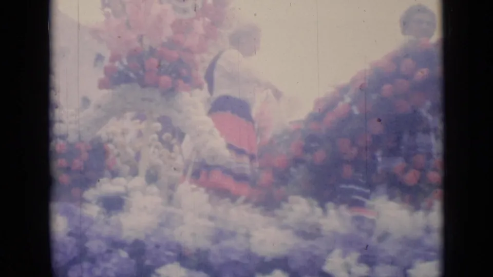 A flower-covered parade float in Cannes shows red and pale blooms with small flags and bright 8mm exposure in the street scene.