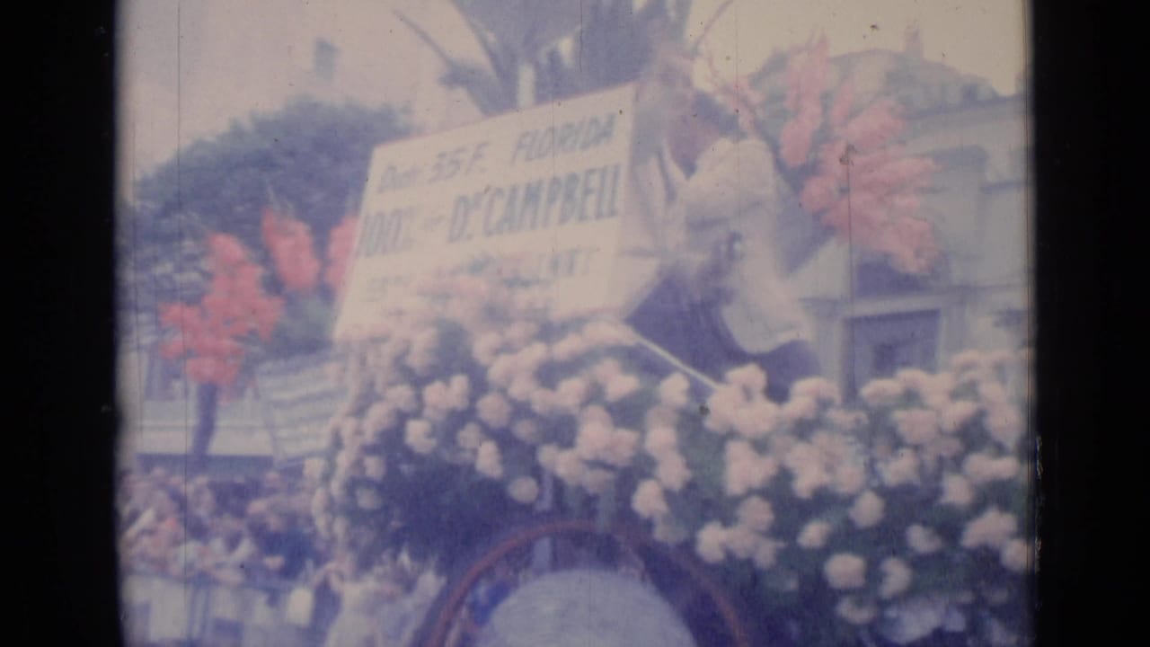 Flower-covered parade float with a large Florida Dr. Campbell sign and spectators nearby.
