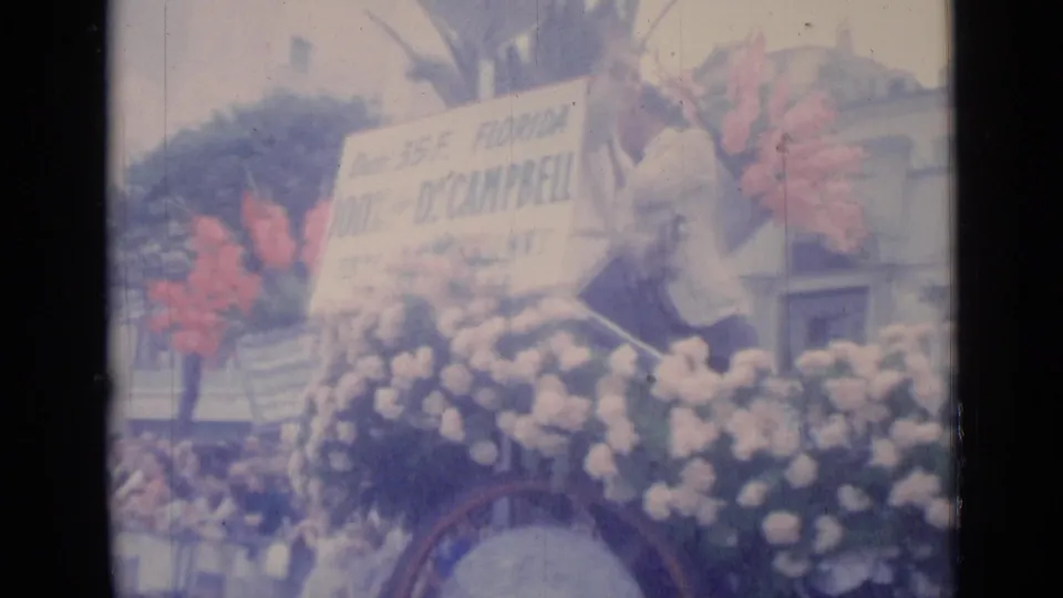 1962 Cannes home-movie frame showing a floral parade float with a Florida Dr. Campbell sign and people gathered along the street.