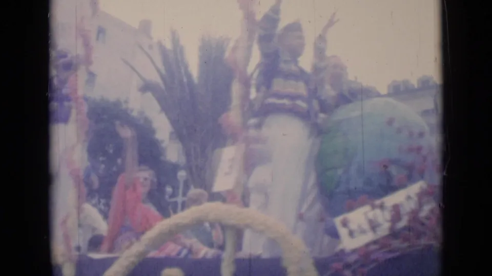 1962 Cannes parade view of float riders near a globe-like decoration, palm-style foliage, and spectators in a soft 8mm color frame.