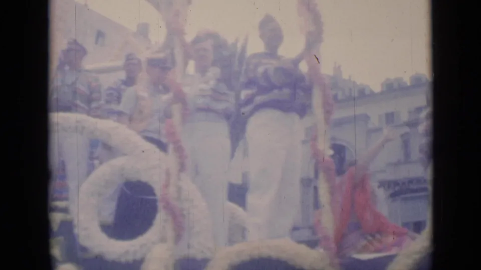 Cannes 1962 home-movie frame showing people on a decorated parade float, a globe prop, and a waving spectator at street level.