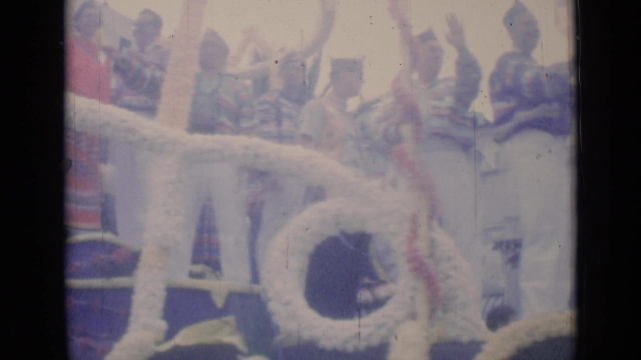 1962 Cannes home-movie frame showing people on a decorated parade float, with striped shirts, hats, and soft faded 8mm color.