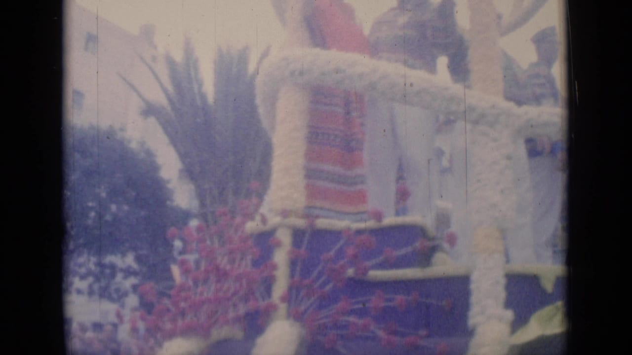 Parade float detail with striped fabric, floral decoration, and people partly visible at the top.