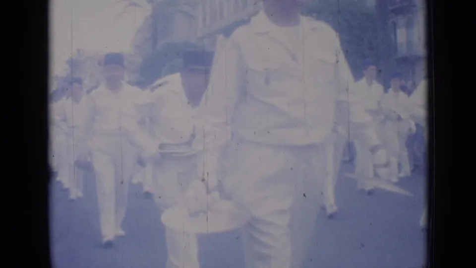 Cannes parade footage shows white-uniformed band members and drummers moving past a handheld 8mm camera.