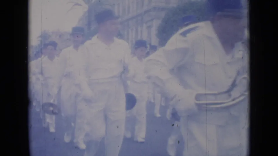 1962 Cannes street parade frame with uniformed musicians passing close to the camera and spectators behind them.