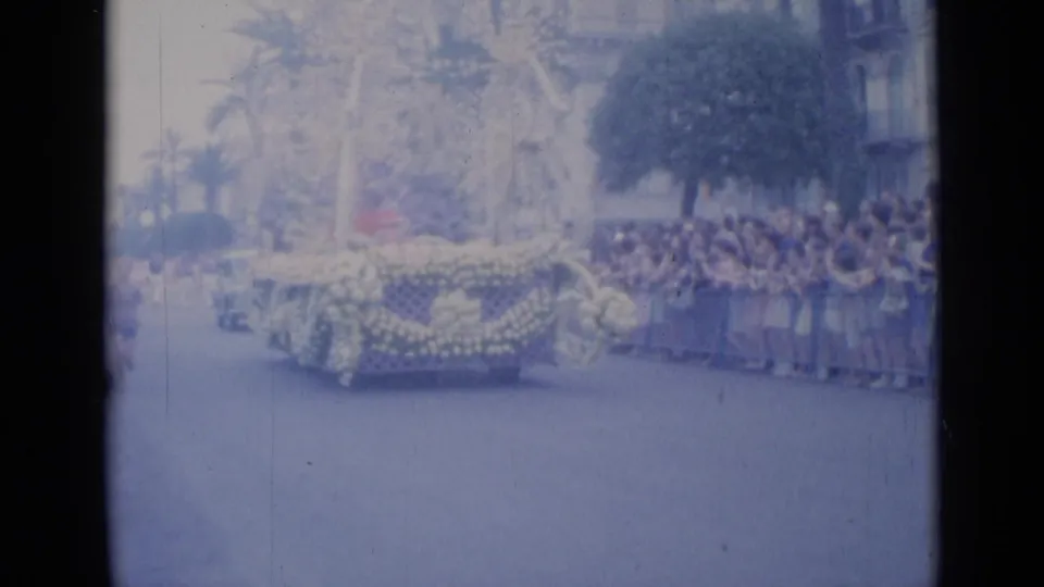 Cannes 1962 home-movie frame showing a floral parade float on the street with spectators gathered along the route.