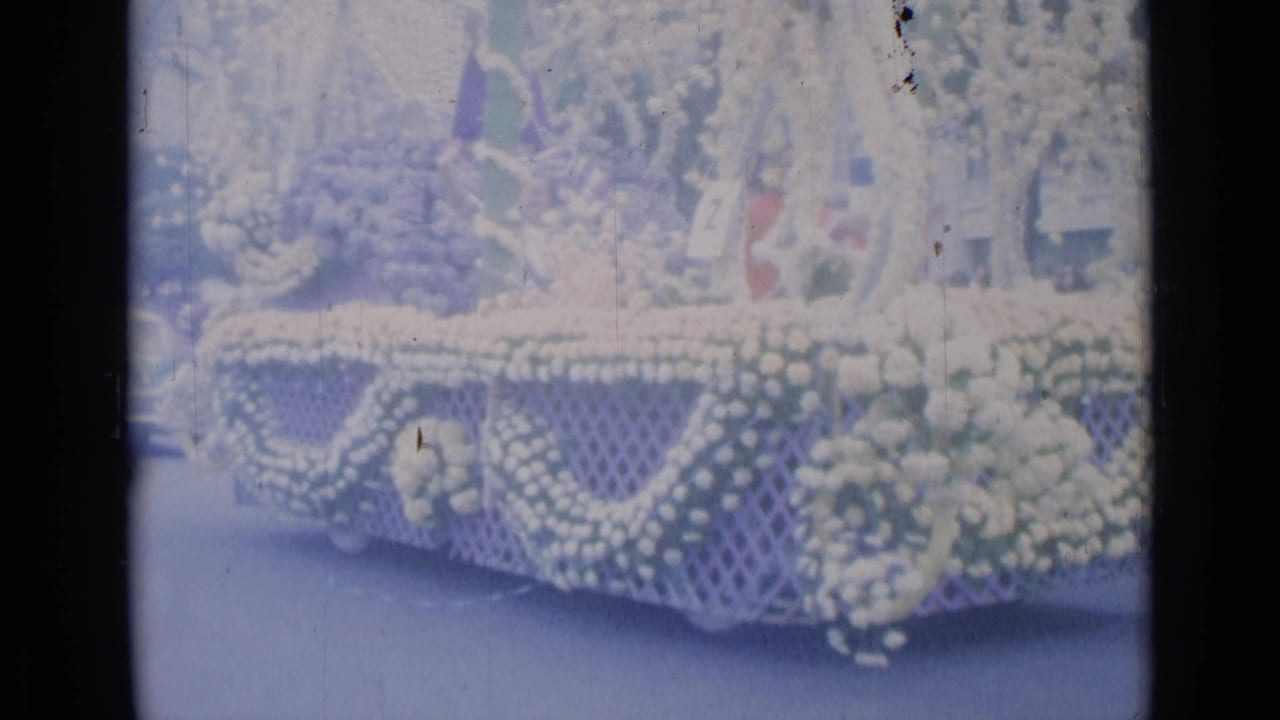Floral parade float with white flowers, greenery, lattice panels, and a number placard.
