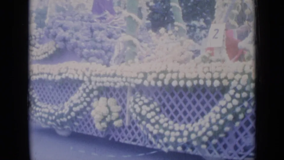 Close 8mm view of the Cannes floral parade float, showing heavy white flower decoration, greenery, latticework, and the number 2 sign.