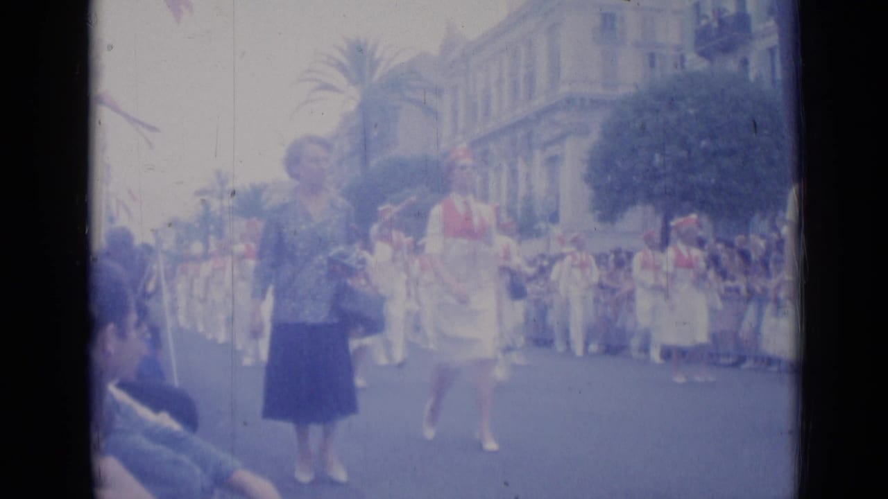 Marching parade participants and spectators on a palm-lined street.