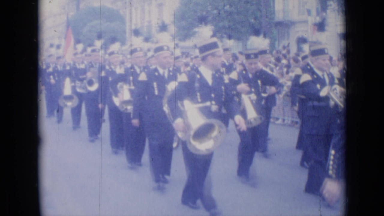 Uniformed marching band advances along a crowded street with brass instruments.