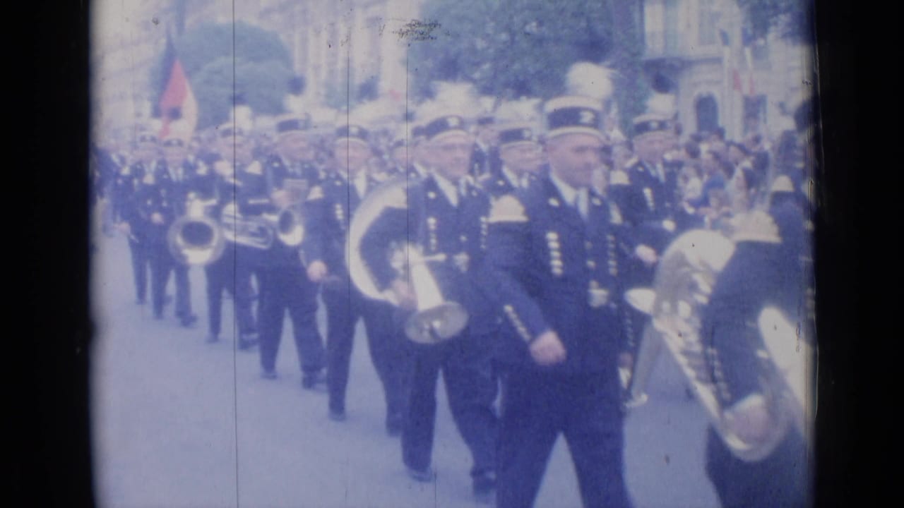 Marching band members in dark uniforms pass close to the camera with large brass horns.