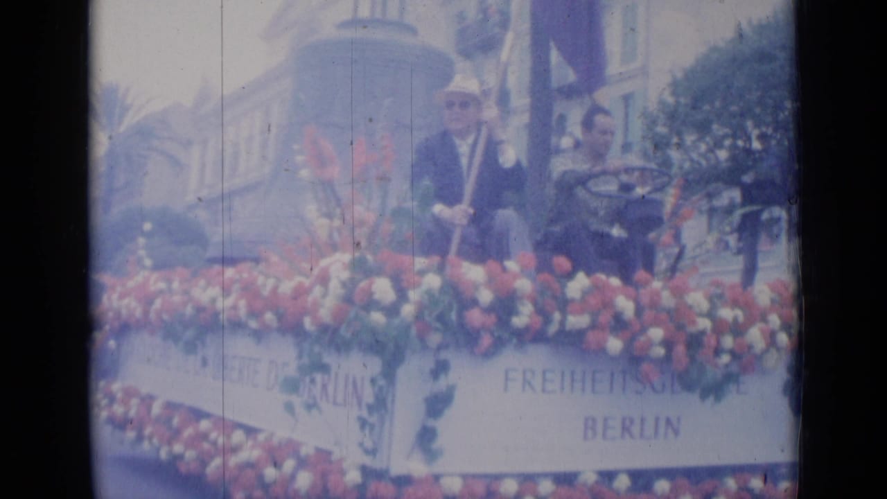 Flower-covered parade float with suited men and Berlin freedom signage.