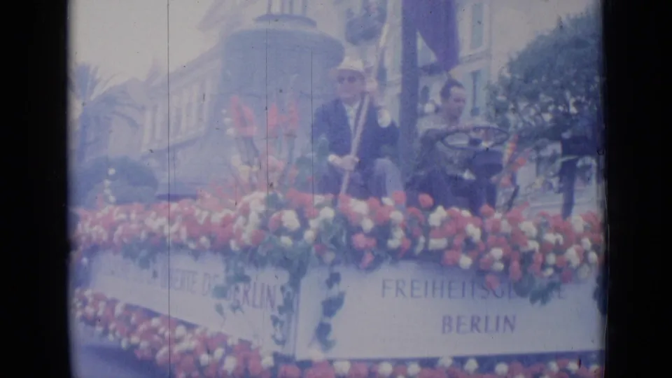 1962 Cannes home-movie frame showing a flower-adorned float with suited men and French-German Berlin freedom text.