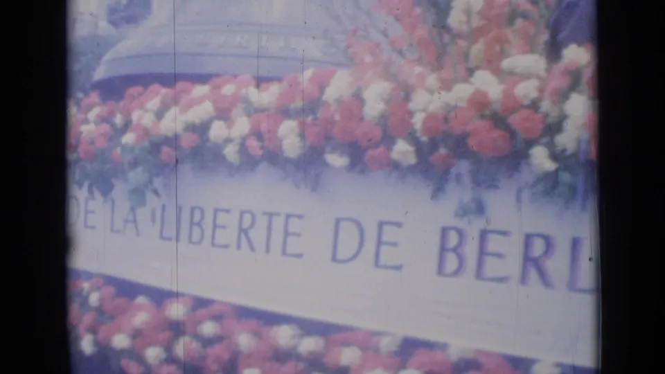 Close 1962 Cannes frame of red and white flowers above French lettering for the Berlin freedom bell on a parade float.