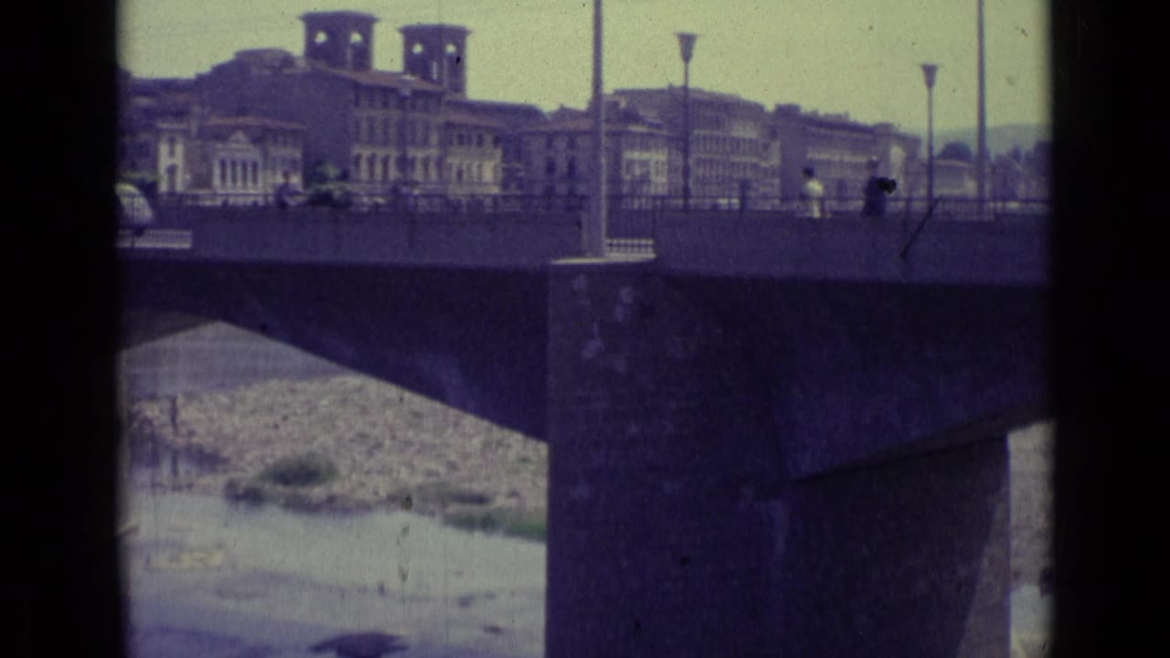 Bridge over a river with buildings and tower-like structures beyond it.