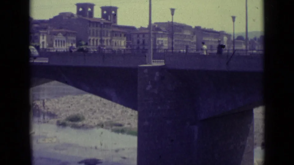 Florence bridge over the river with urban buildings and tower-like structures in the background, seen through a dark 8mm frame edge.