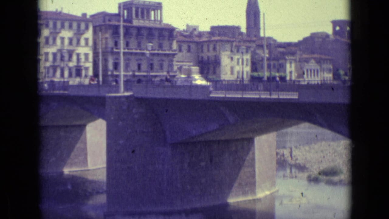 Cars cross a bridge over a river with Florence buildings beyond.