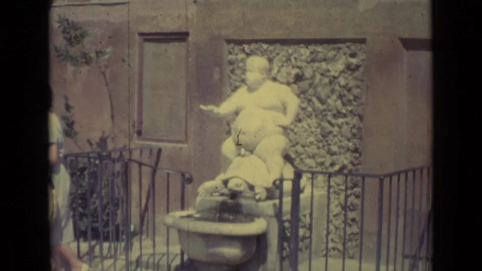 Faded 1962 Florence frame centered on the white seated figure and turtle fountain, with a cropped woman at the left edge.