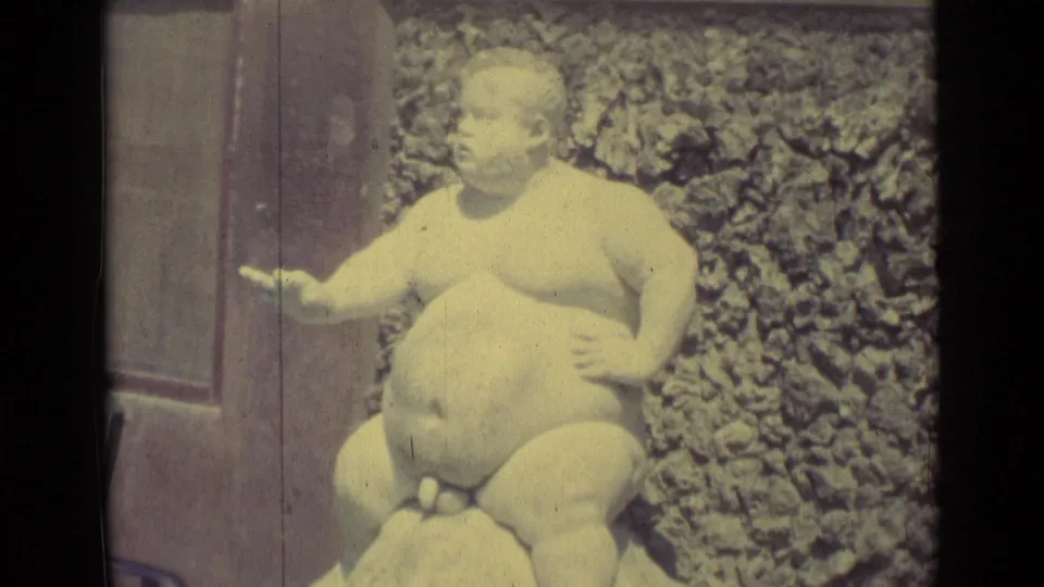Close 8mm view of the white seated figure sculpture on the turtle fountain in Florence, with bright exposure and a textured wall behind it.